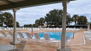 Et poolområde med liggestole og borde, en swimmingpool og palmer i baggrunden.