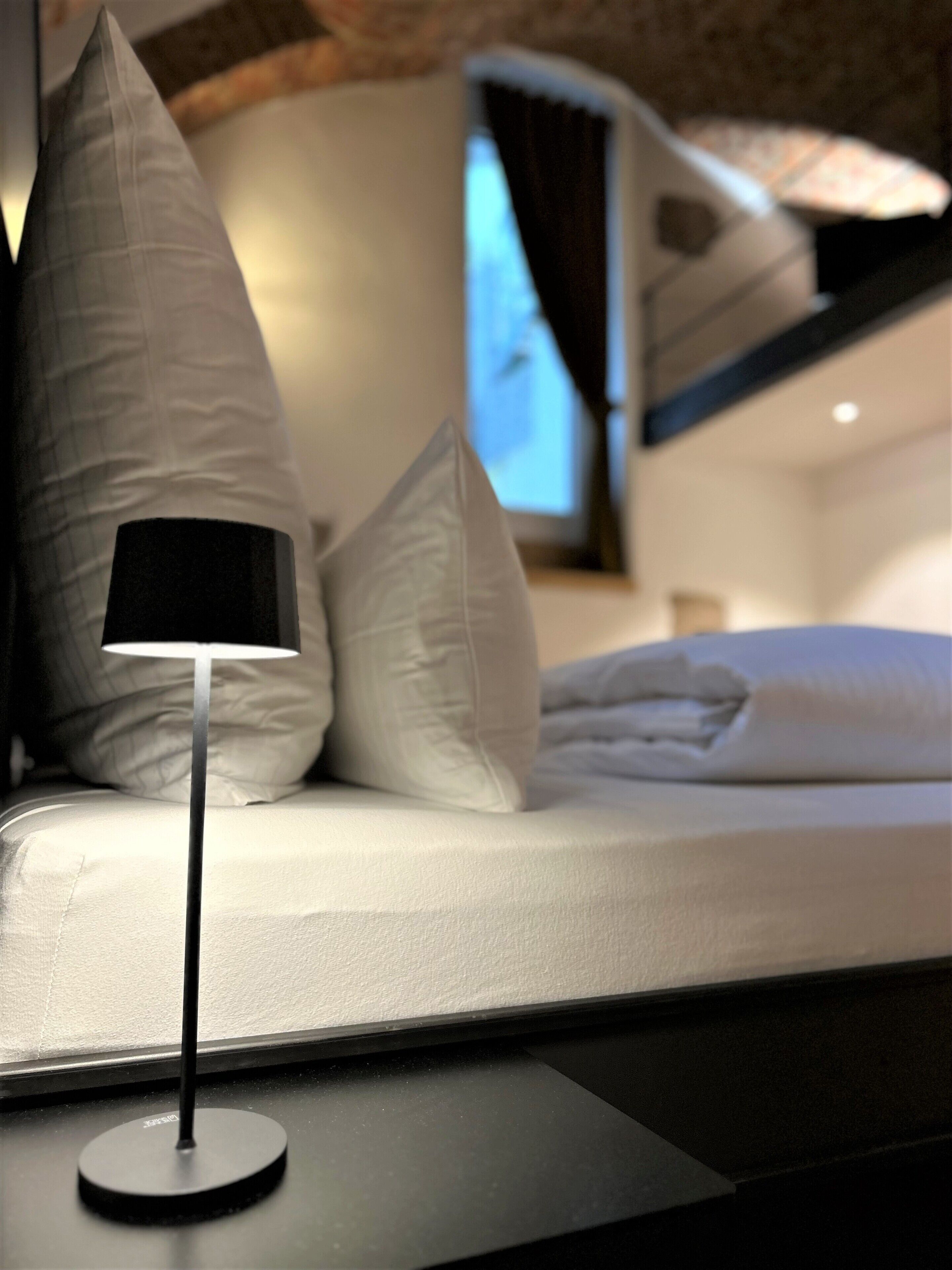 A bed with white bedding and a modern floor lamp.