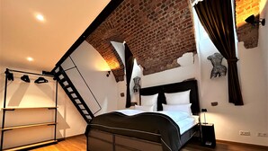 A bedroom with a sloped ceiling, a bed with black headboard, a wooden floor, and a ladder against the wall. - Historical Luxury Homes - Luxus Familien Suite (Freiburg im Breisgau)