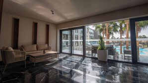 Une chambre d’hôtel moderne dotée d’une grande porte-fenêtre coulissante donnant sur un espace piscine, d’un canapé, d’un fauteuil et d’une table basse.