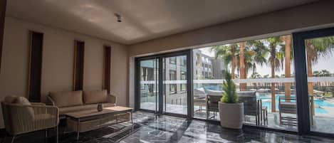 Una habitación de hotel moderna con un gran ventanal corredero que da a una zona de piscina, un sofá, una silla y una mesa de centro.