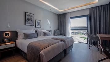 A modern hotel room with two beds, a desk, and a view of the outdoors.
