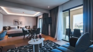 Une chambre d’hôtel moderne équipée d’un lit, d’une télévision, d’un coin repas et d’un balcon offrant une vue sur la ville.