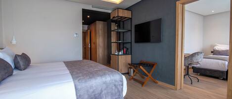A modern bedroom with a large bed, a wooden wardrobe, a TV mounted on the wall, and a small seating area.