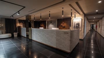 Een receptiegedeelte met een modern ontwerp, met een receptiebalie, hangende verlichting en een groot poster aan de muur.
