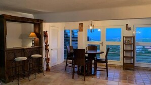 A dining area with a table and chairs, a bar with stools, a decorative wall piece, and large windows with a view. - Buck Island Views on North Shore: Mermaid & View (Christiansted)