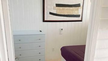 Een slaapkamer met een bed, een dressoir, een plafondventilator en een abstract schilderij in een lijst aan de muur.