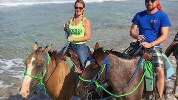 Two people riding horses on a beach with ocean waves in the background.