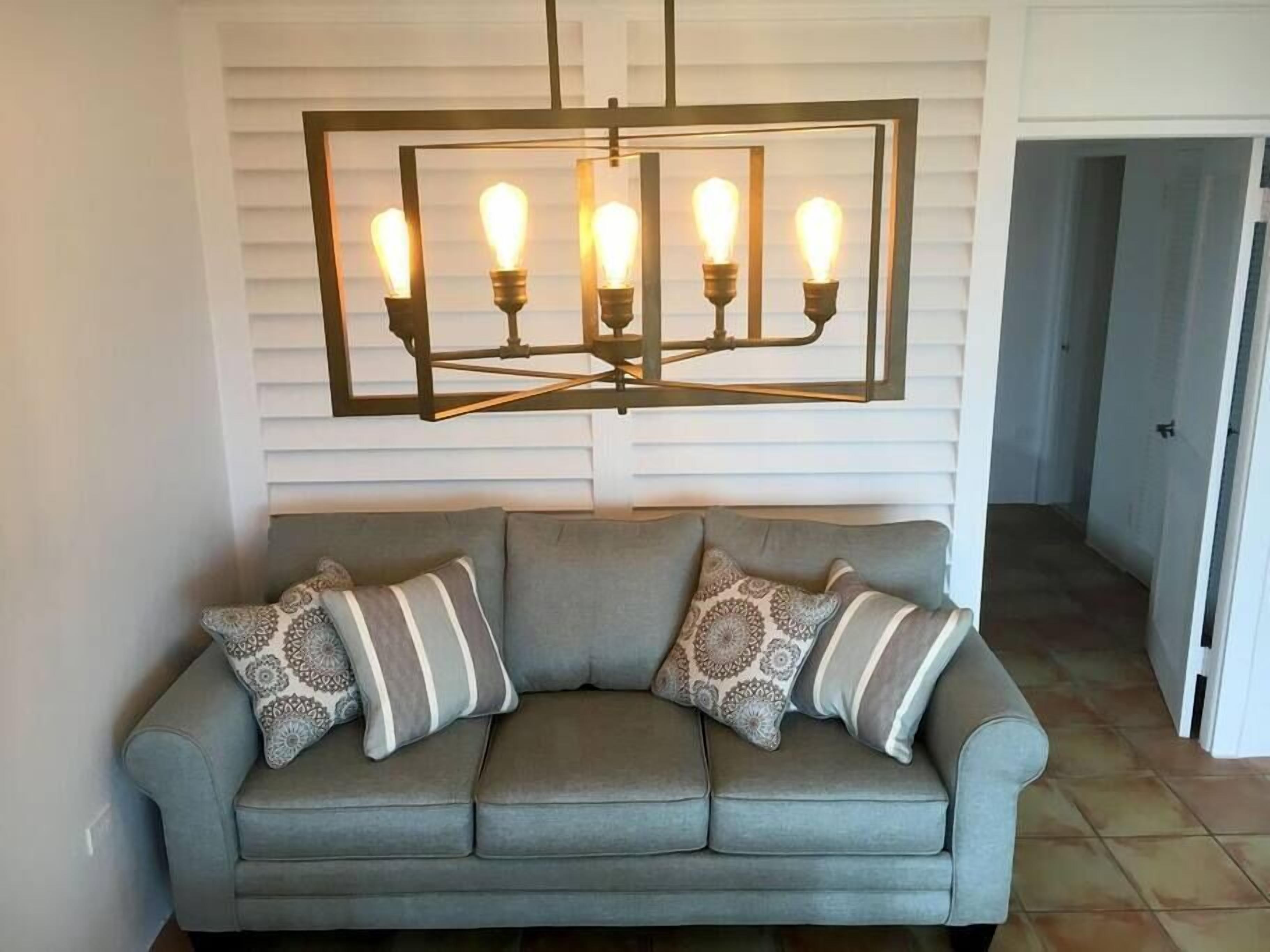 A gray sofa with patterned cushions and a modern light fixture above it.