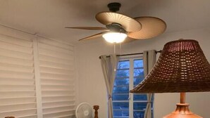 Une chambre à coucher avec un lit, un ventilateur de plafond, une lampe et une fenêtre avec des rideaux.