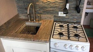 Uma cozinha com bancada de granito, pia com torneira, fogão e painel atrás do fogão com padrão de pedra.
