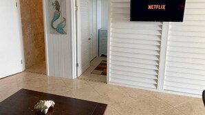 A room with a television displaying 'NETFLIX', a decorative mermaid tail on the wall, and a tiled floor. - Buck Island View N. Shore: View, Mermaid, Windsors (Northcentral)
