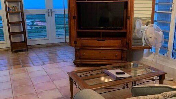 A living room with a wooden entertainment center, a glass coffee table, and a sofa. - Buck Island View N. Shore: View, Mermaid, Windsors (Northcentral)