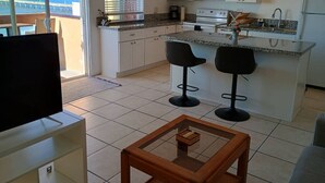 Eine moderne Küche mit einer großen Kochinsel, zwei Barhocker und einem Fernseher im Wohnbereich.
