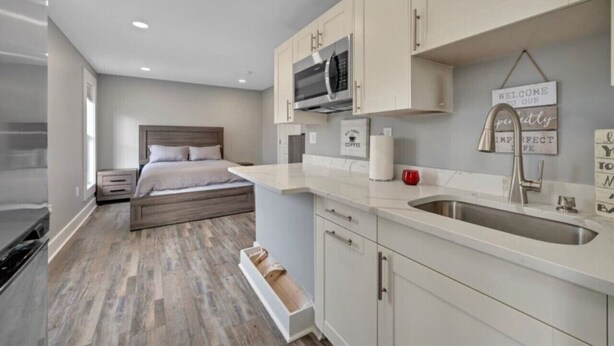 A compact bedroom with a bed and a nightstand, a kitchenette with a microwave, and a sink. - Downtown Studio Loft directly on Front St (Traverse City)