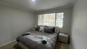 Une chambre à coucher avec un lit, une table de chevet, une fenêtre avec des stores et une vue sur l’extérieur.