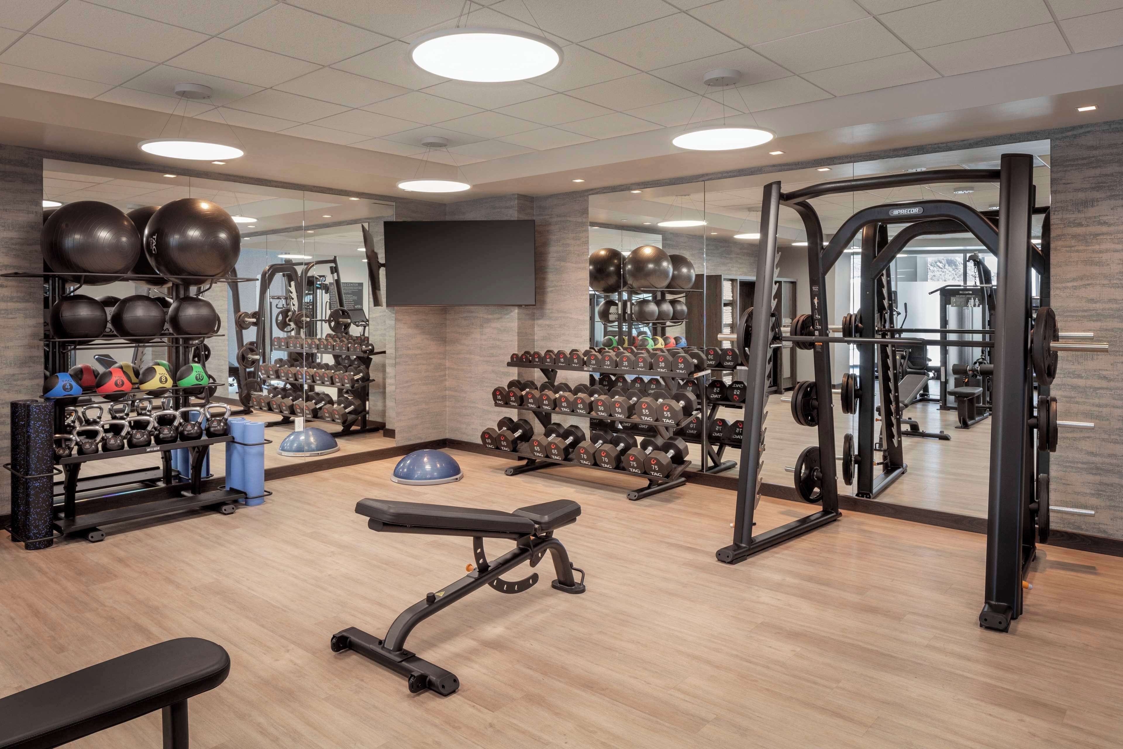 A gym with exercise equipment, benches, and a mirrored wall.