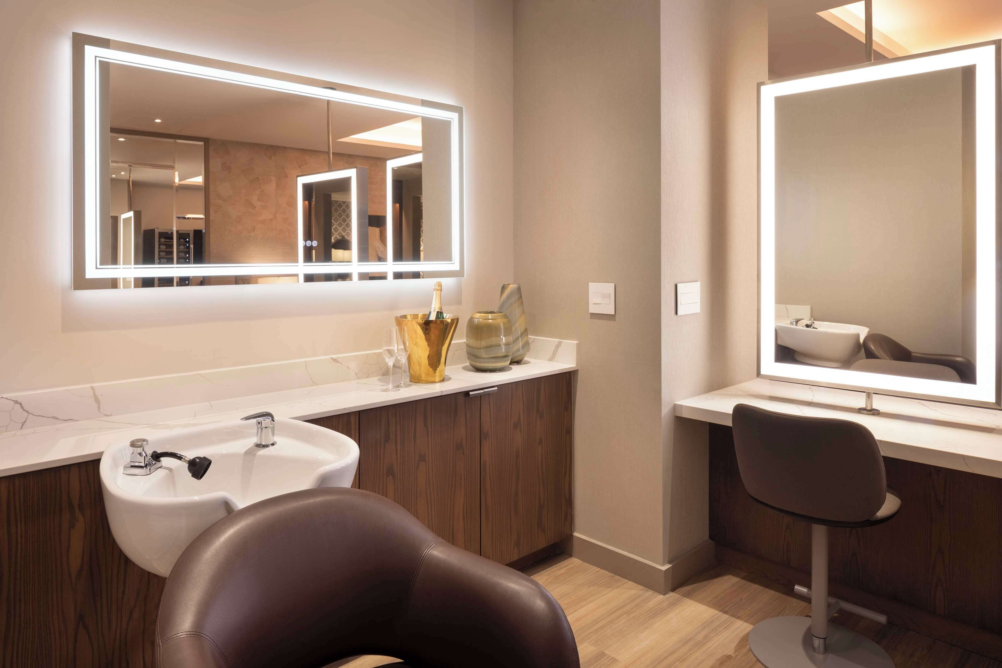 A modern bathroom with a large mirror, a sink, and a chair.