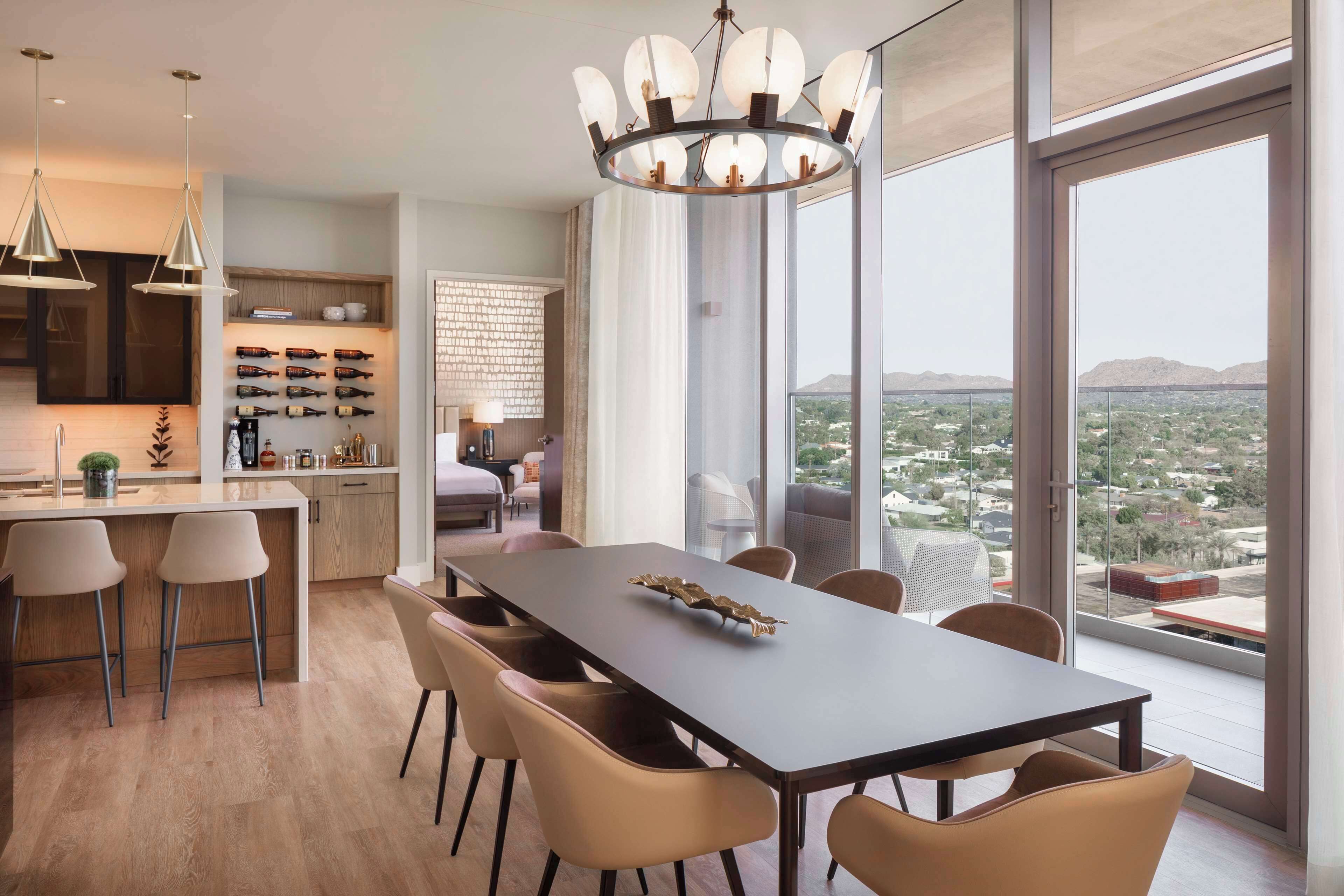 A modern dining area with a large table and chairs, a chandelier, and a view of the cityscape through large windows.