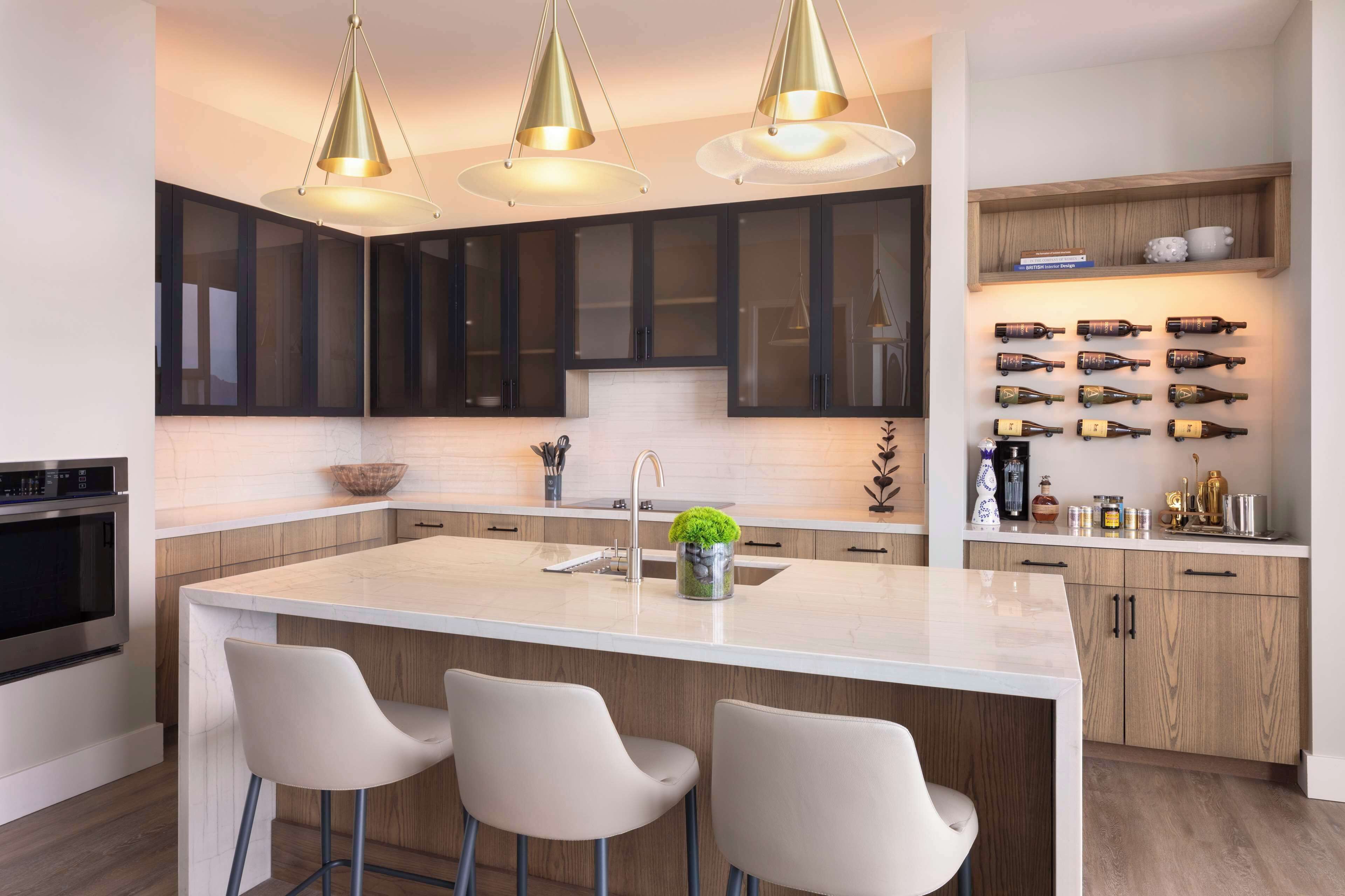 A modern kitchen with a central island, bar stools, pendant lighting, and a wine rack.