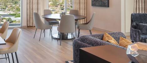 A modern hotel room with a dining area, a sofa, and a view of a mountainous landscape.