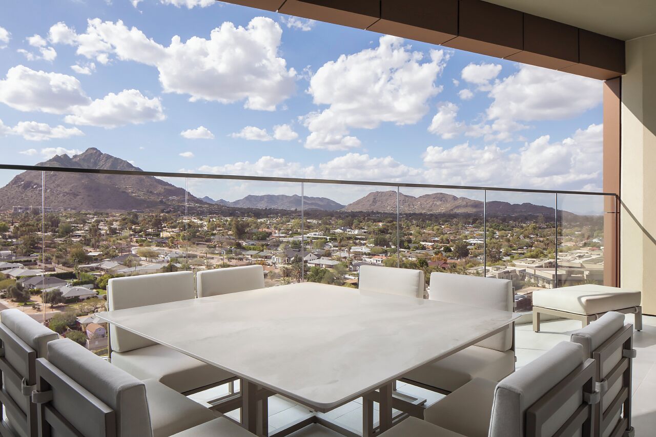 Un balcón con mesa y sillas, que ofrece vistas a un paisaje montañoso y una zona residencial.