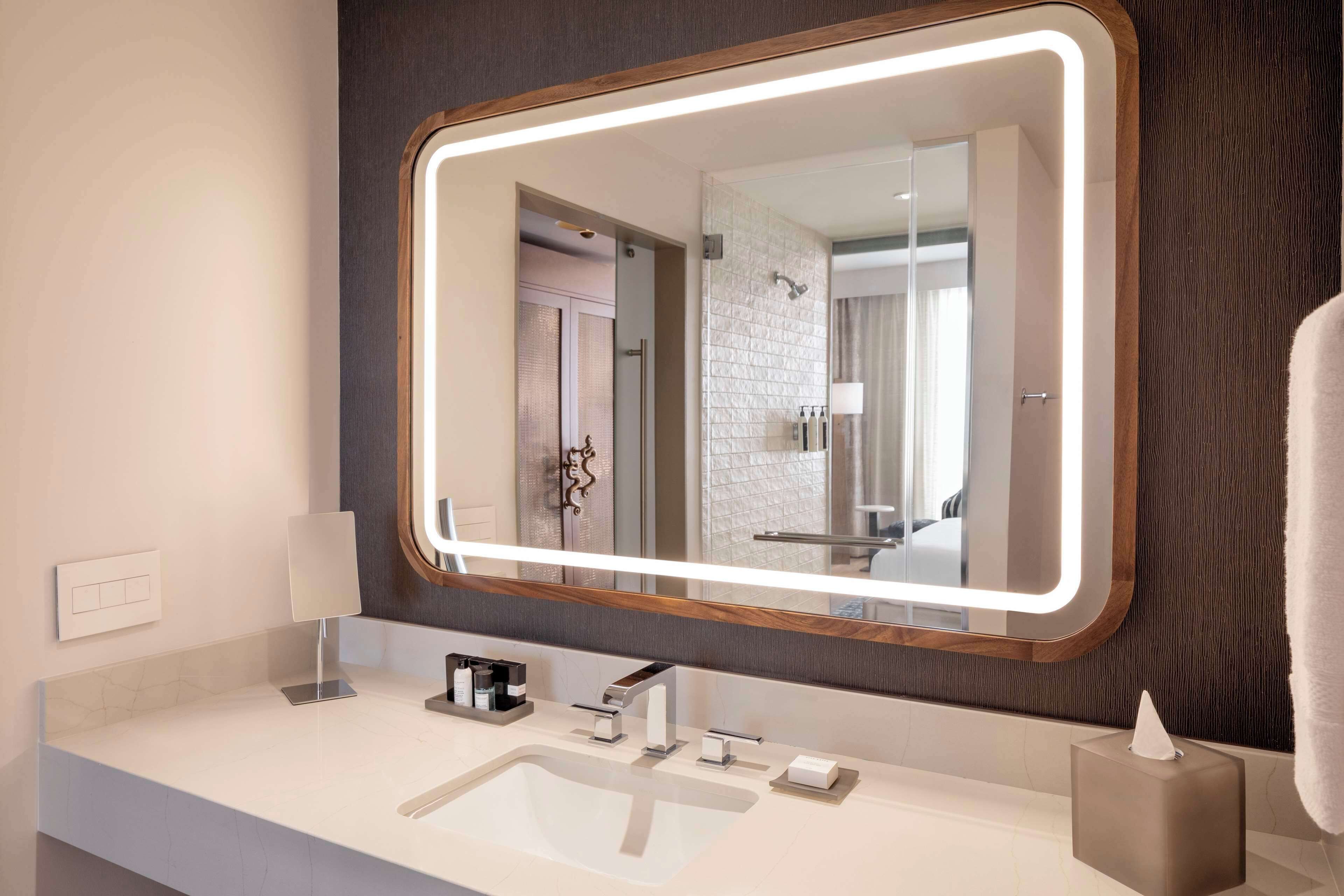 Un baño moderno con un espejo grande, un lavamanos blanco y un perchero para toallas.