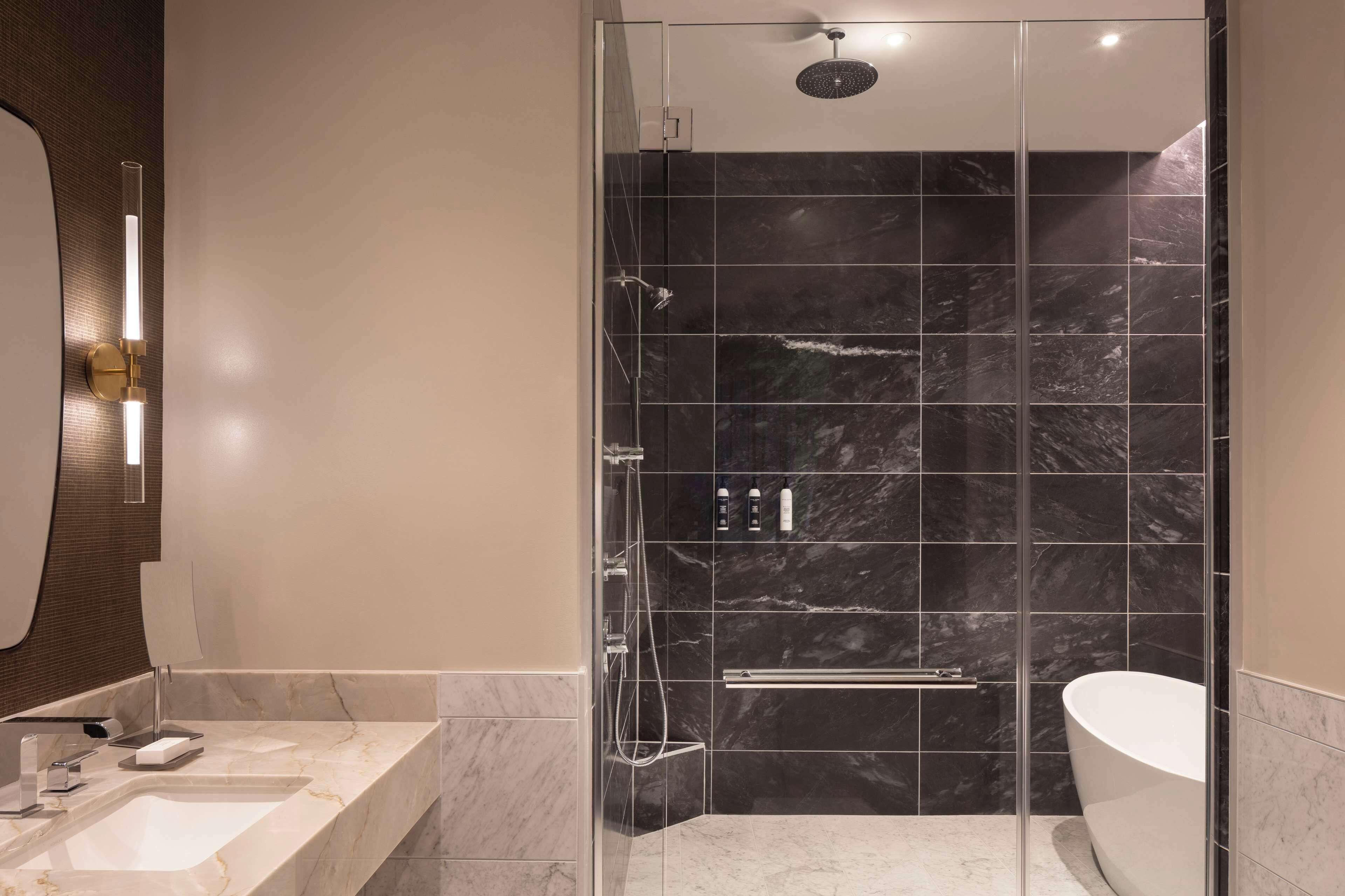 A modern bathroom with a glass-enclosed shower, a freestanding bathtub, and a marble countertop sink.