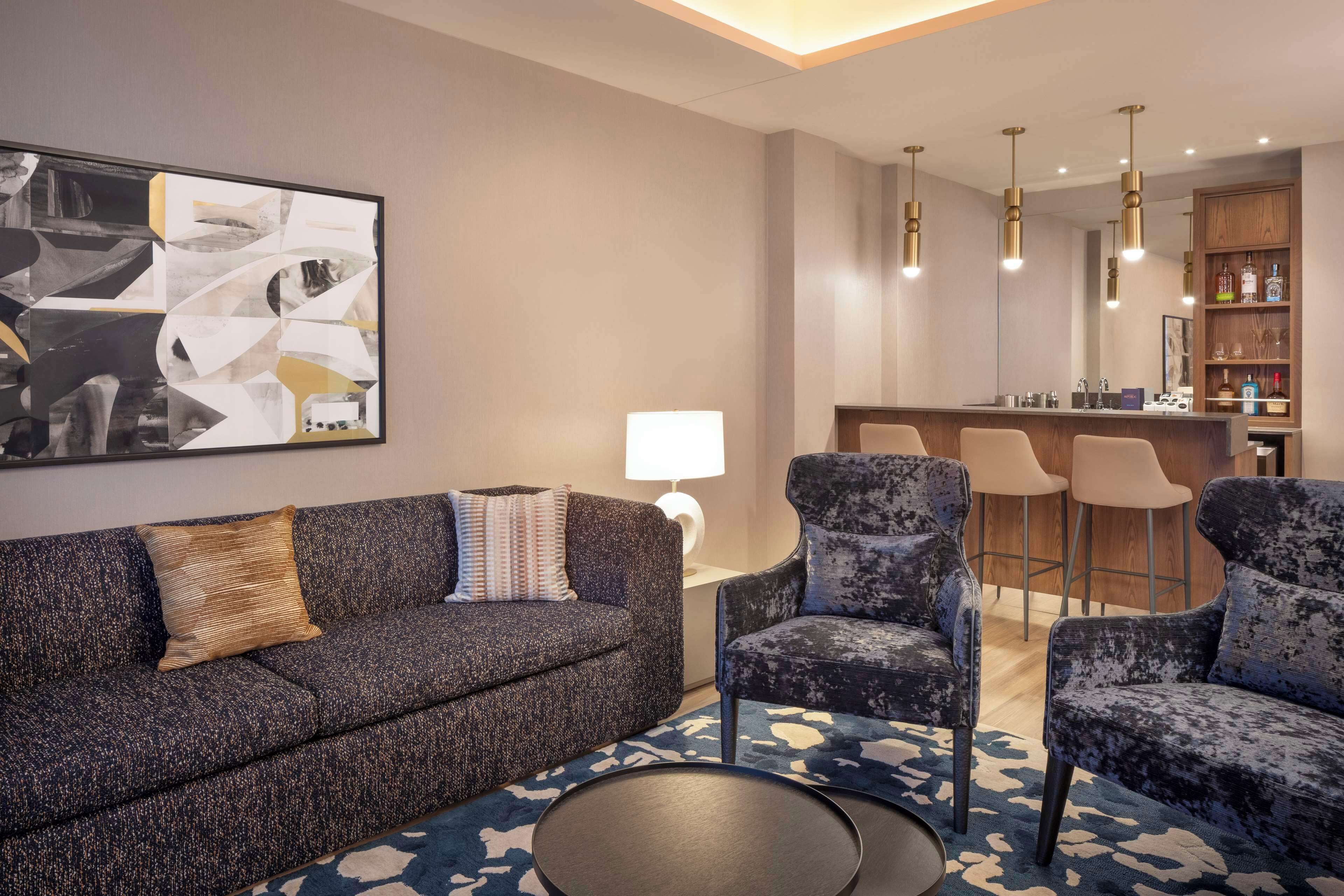 A modern living room with a dark grey sofa, two armchairs, a round coffee table, and a large abstract painting on the wall.