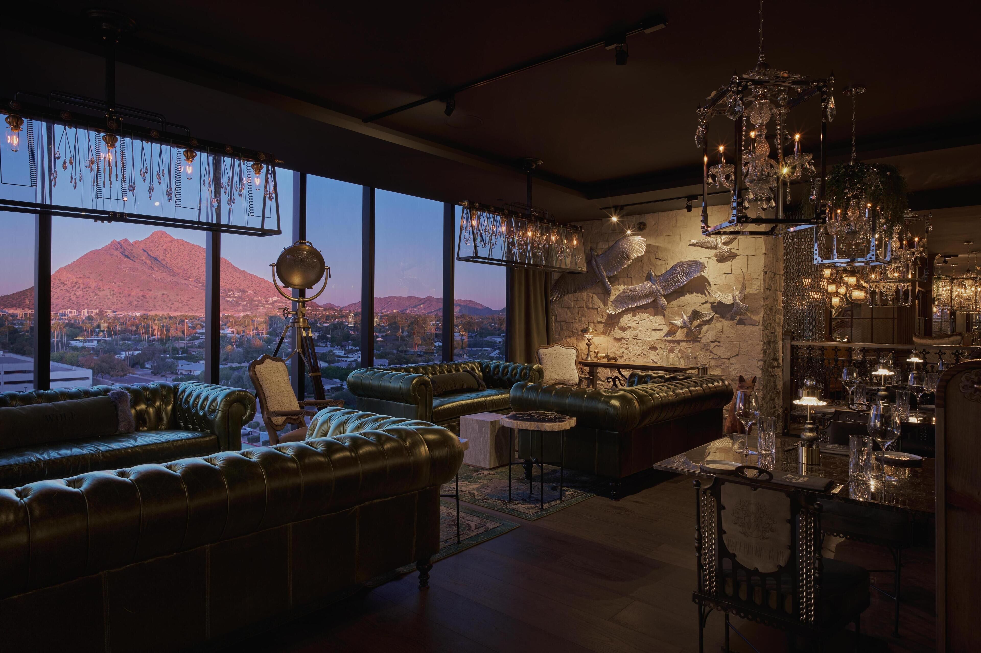 A spacious living room with leather sofas, a dining table set with glasses, and a large window offering a mountain view.
