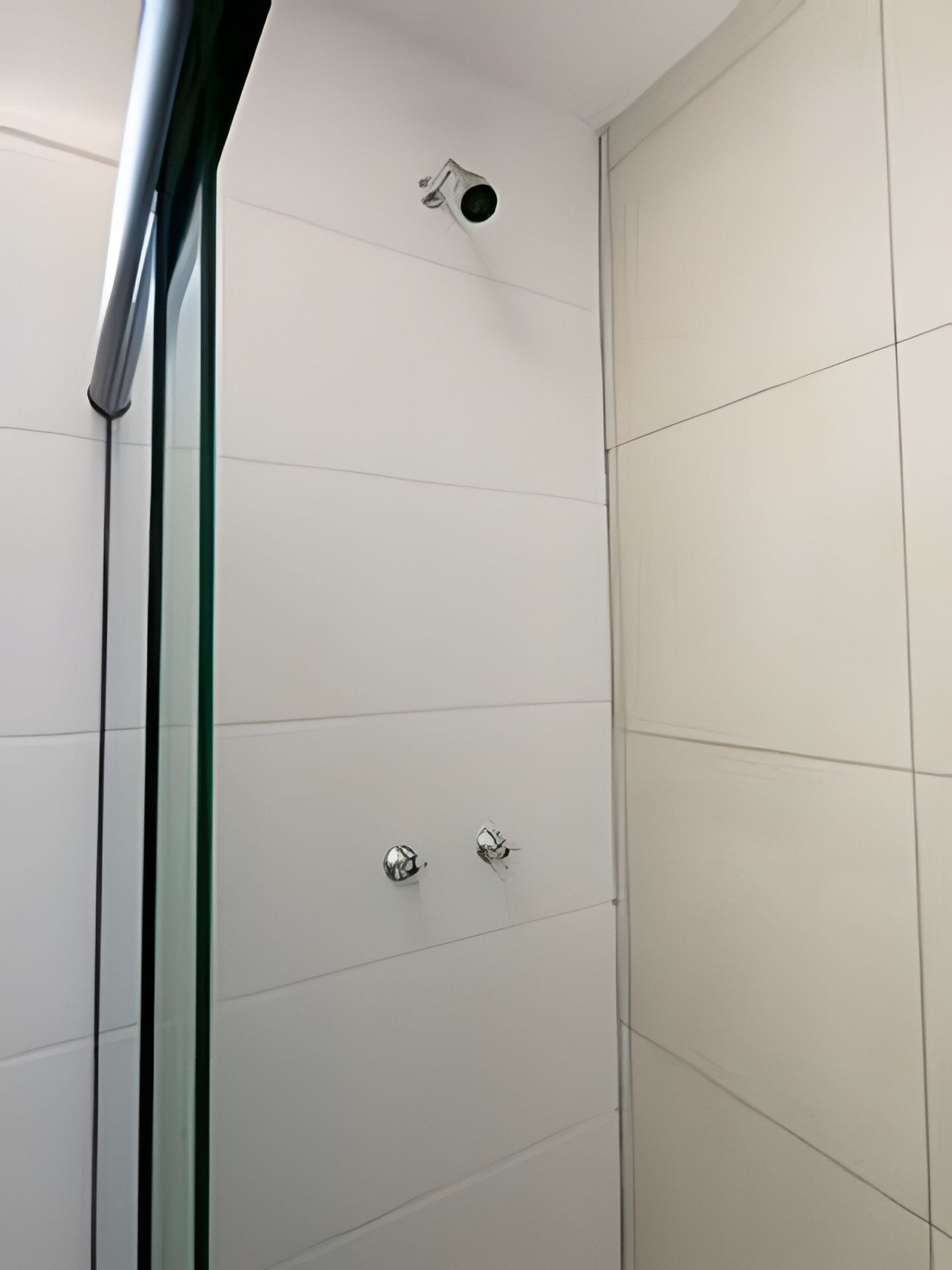 Eine moderne Dusche mit Glastür, einer sichtbaren Duschbrause und zwei chromfarbenen Armaturen.