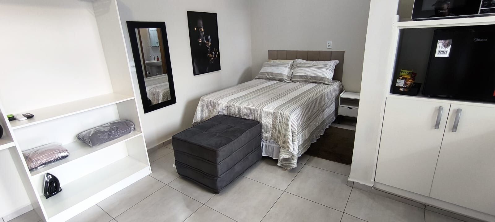 Une chambre à coucher de taille réduite, comprenant un lit, un petit banc, une armoire et un miroir.
