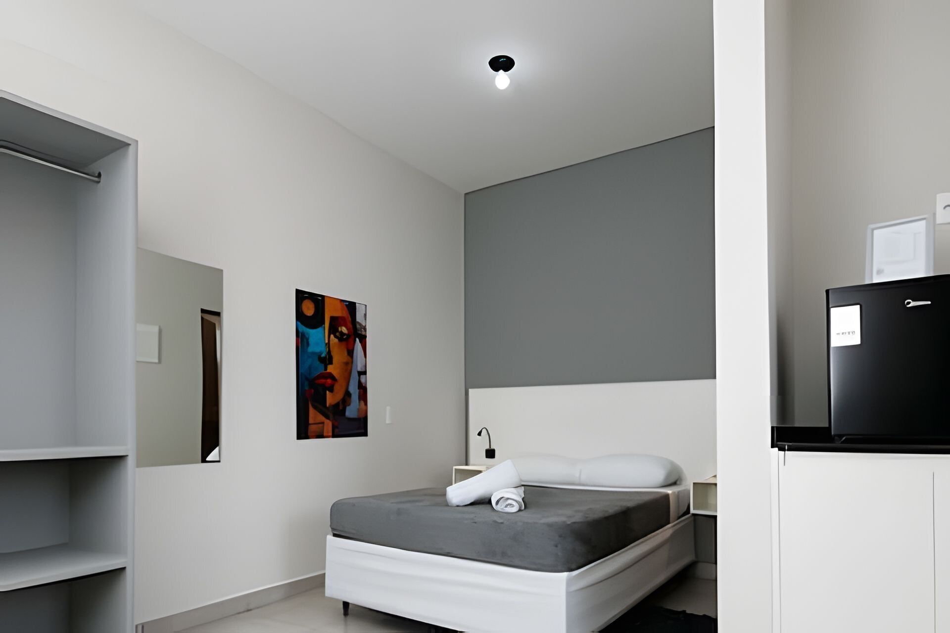 A modern bedroom with a bed, a nightstand, a dresser, a mirror, and a painting on the wall.