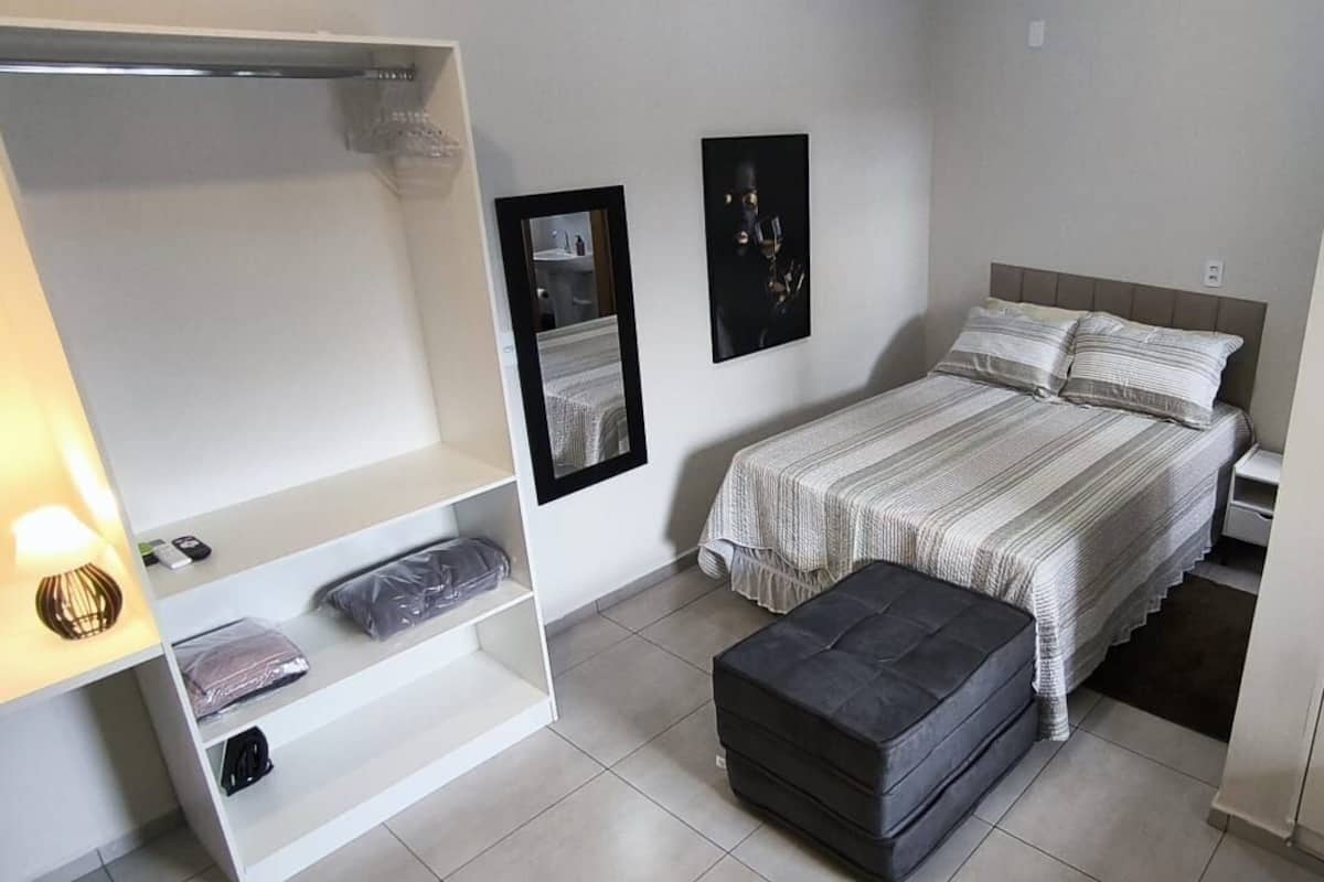 A compact bedroom with a bed, a small seating area, a wardrobe, and a microwave.