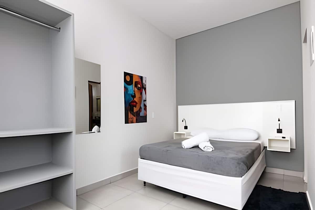 A modern bedroom with a grey bed, white headboard, and a painting on the wall.
