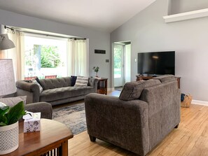 A modern living room with a grey sofa, a wooden coffee table, and a flat-screen TV. - Hot Tub Backyard Oasis Espresso Maker Coffee Bar (South Bend)