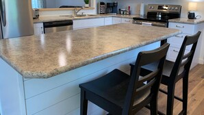A modern kitchen with white cabinets, a granite countertop, stainless steel appliances, and a bar seating area. - HOT TUB Beauitiful Backyard Oasis Newly Renovated (Middlebury)