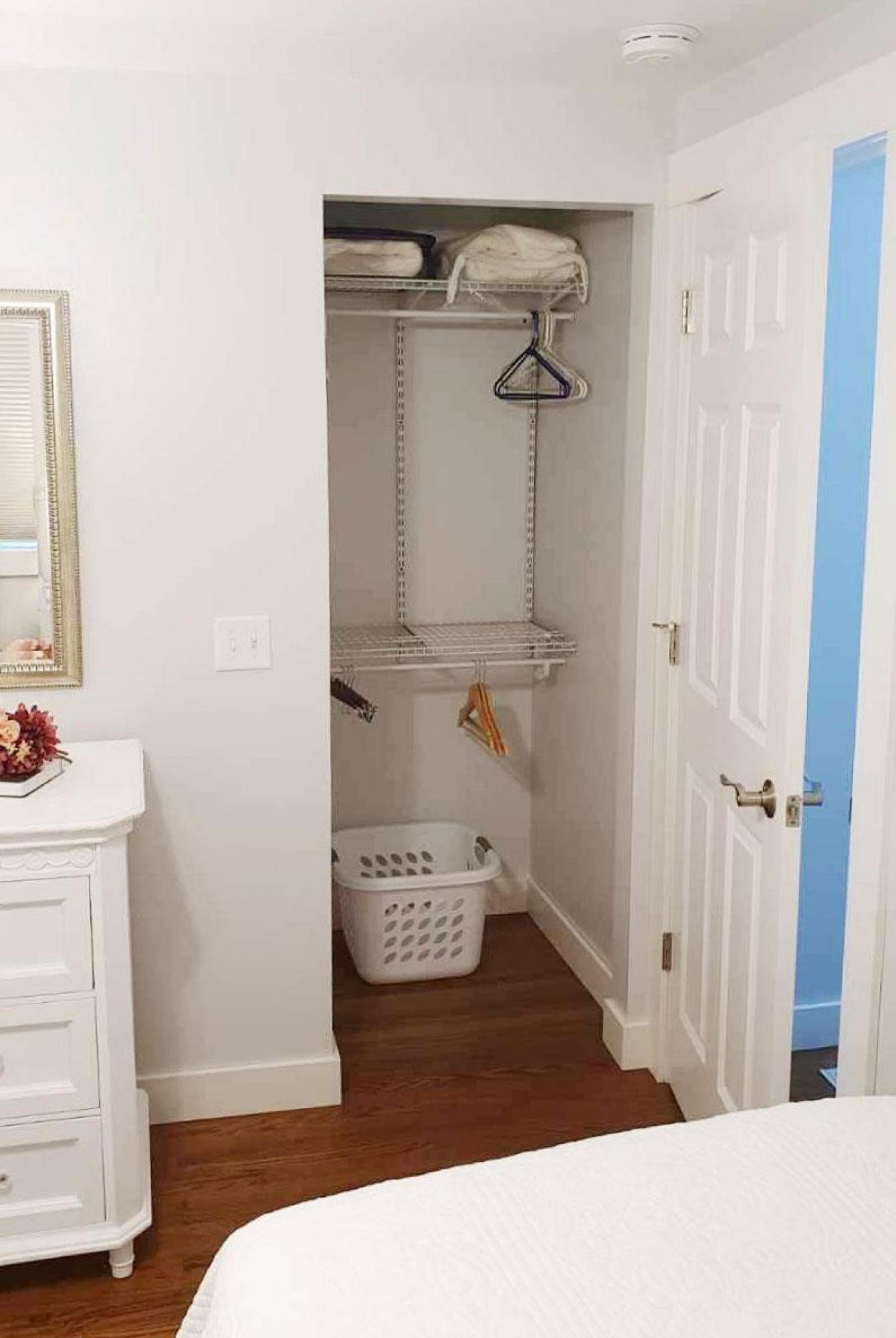 A bedroom with a bed, a dresser, a closet with shelves, and a laundry basket.