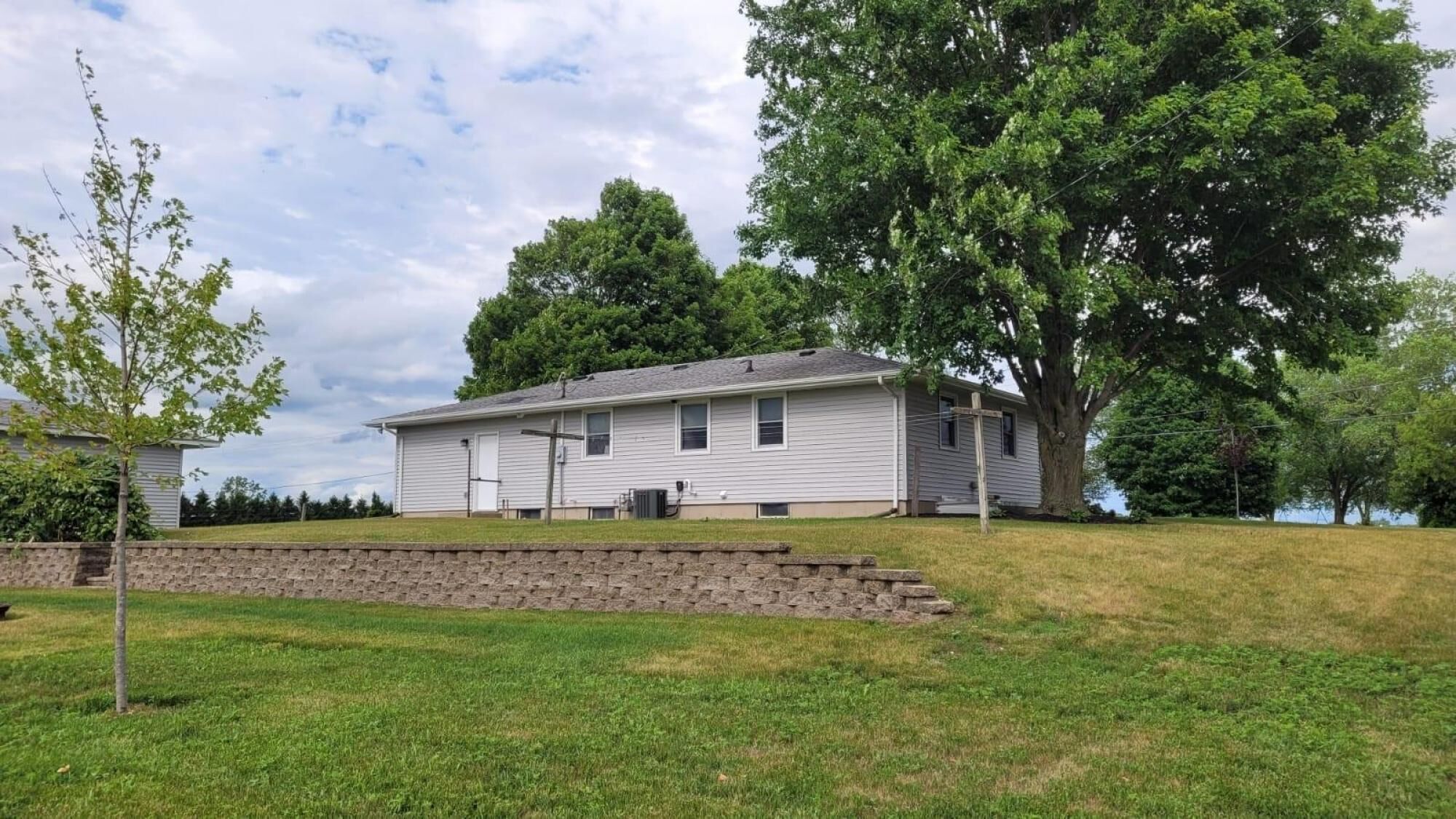 Et etplanshus med en veranda, en støttemur af sten og et stort træ i baggrunden.