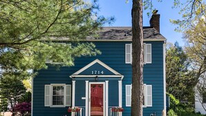 A two-story house with a red door and white shutters, surrounded by greenery and a tree. - HOT TUB 1 2MI to ND Espresso Maker Coffee Bar (South Bend)