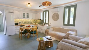 A modern kitchen with white cabinets, a dining table with chairs, and a sofa in a living area. - Unity Villa
 (KEFALONIA)