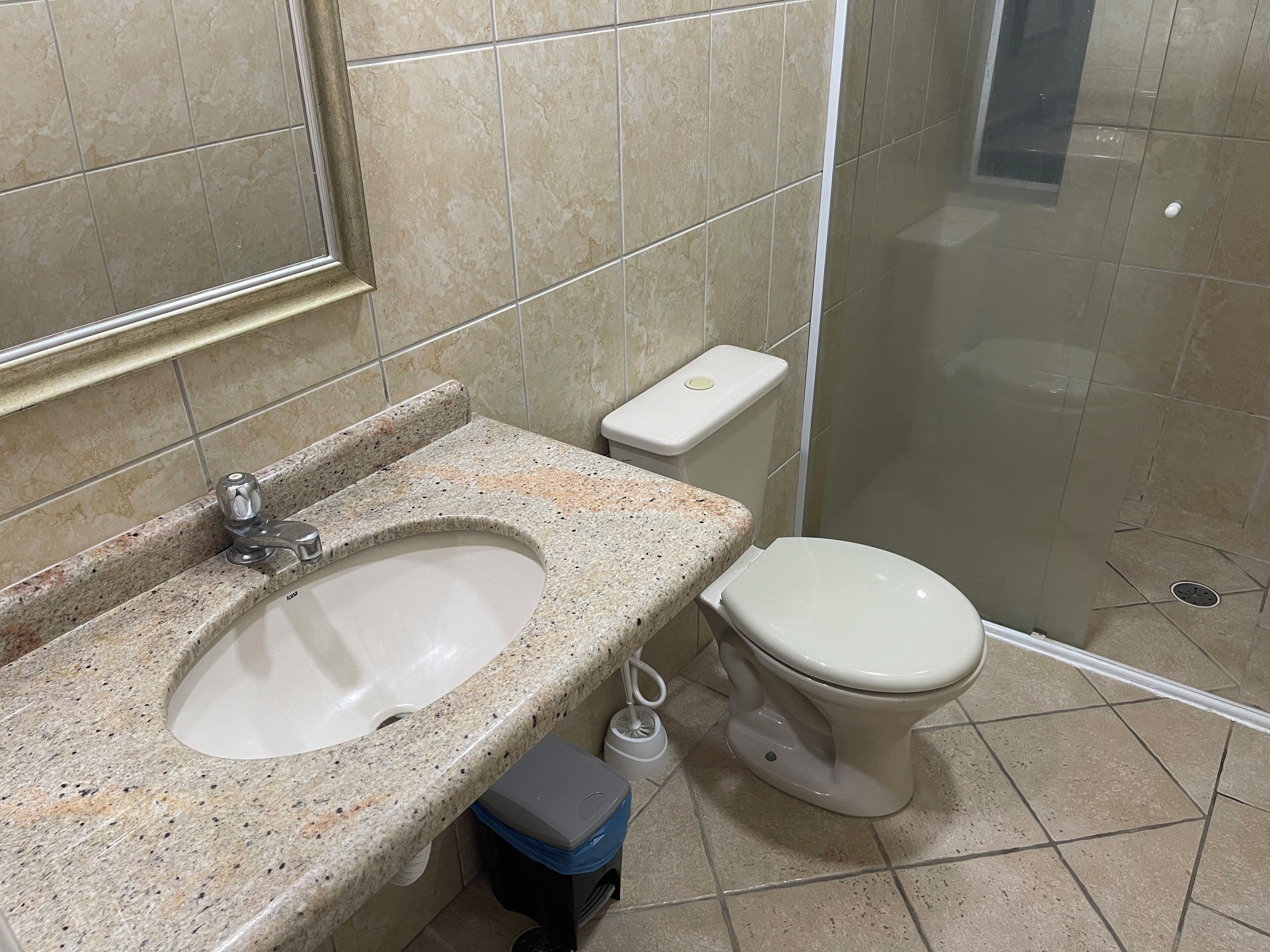 A bathroom with a granite sink, a toilet, and a shower.