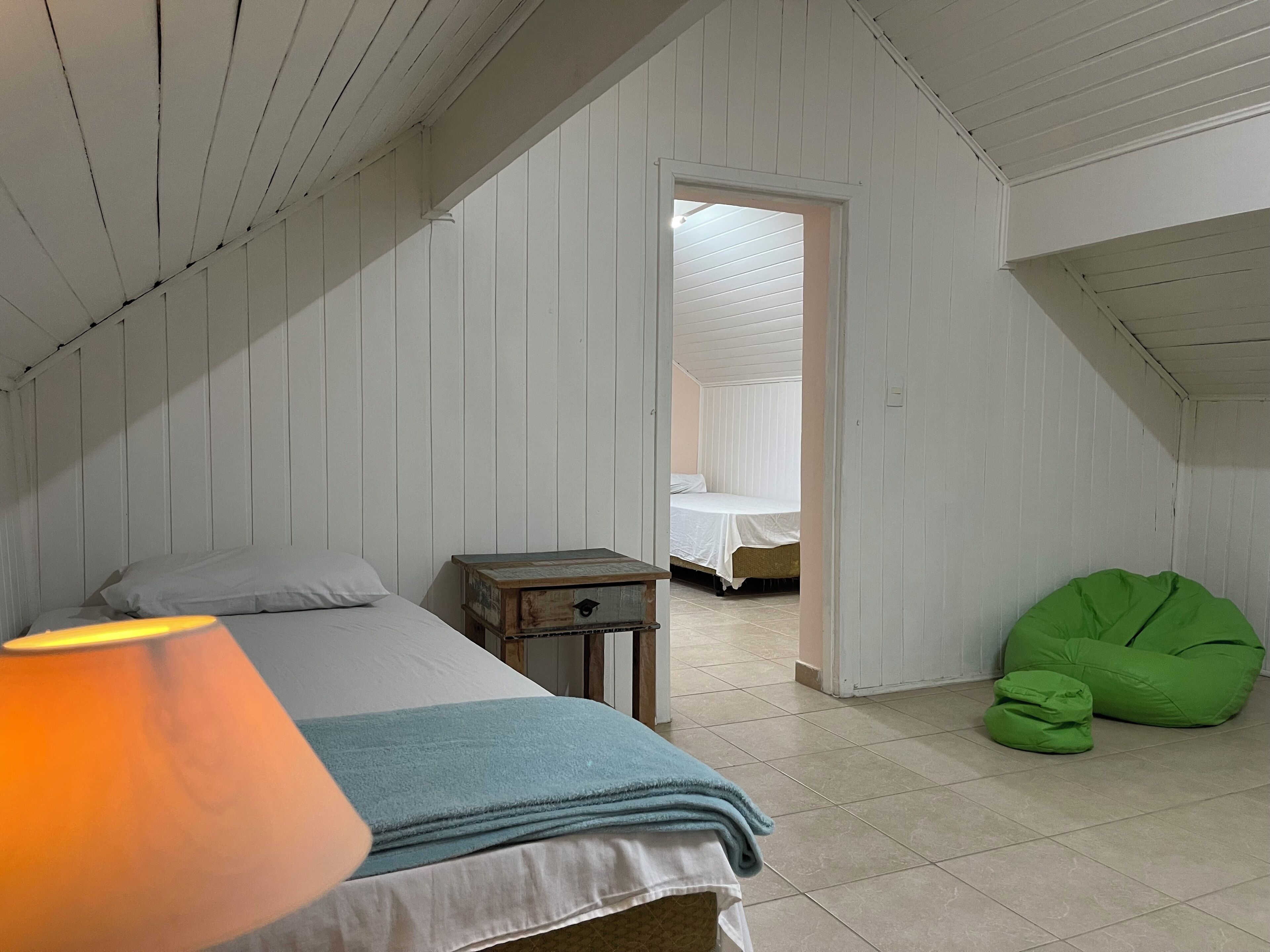 Un dormitorio con cama, mesita de noche, un sillón de mimbre y una lámpara.