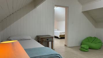 Un dormitorio con cama, mesita de noche, un sillón de mimbre y una lámpara.