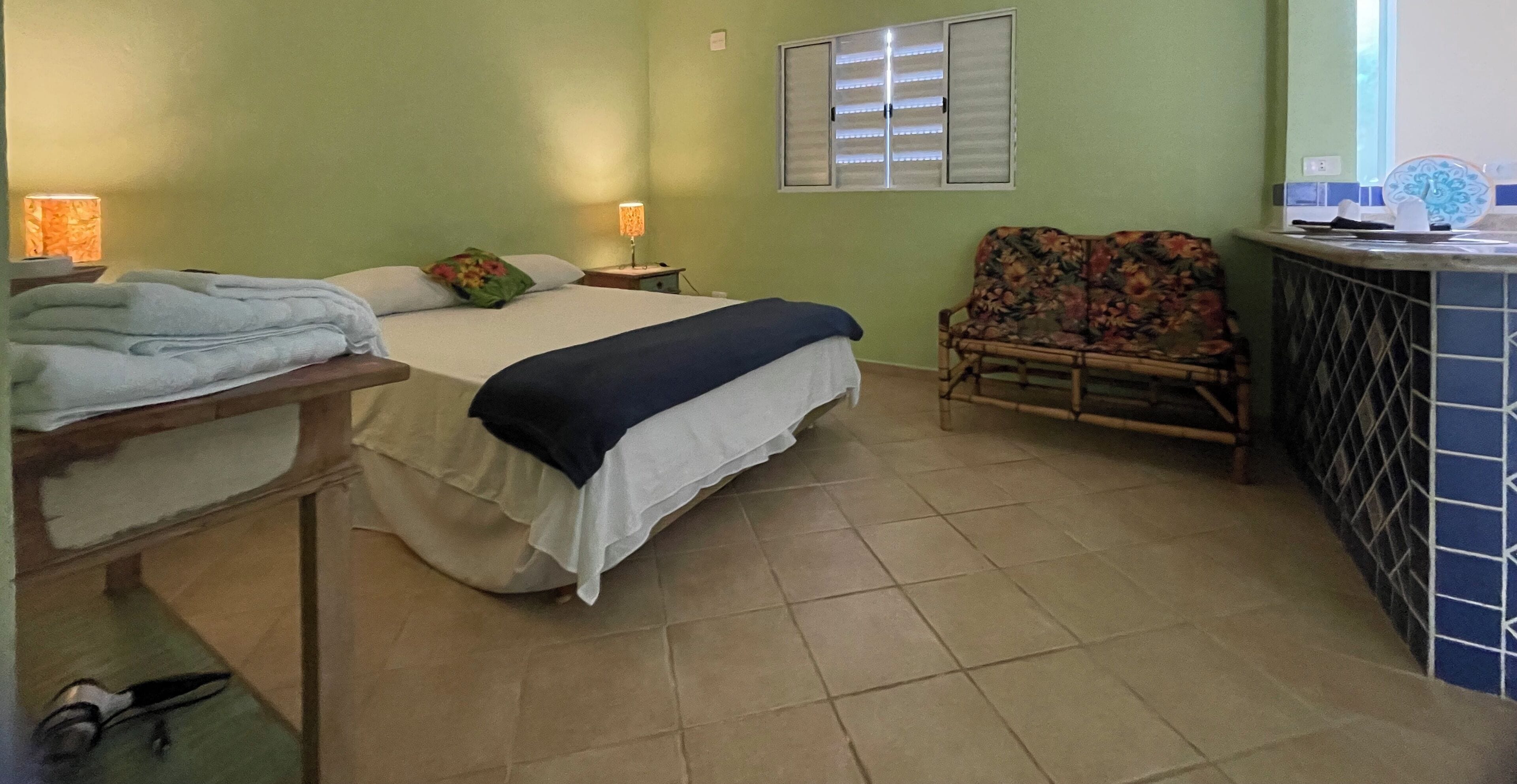 A bedroom with a bed, a nightstand, a chair, and a small table with a lamp.