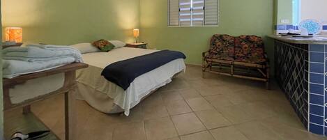 A bedroom with a bed, a nightstand, a chair, and a small table with a lamp.