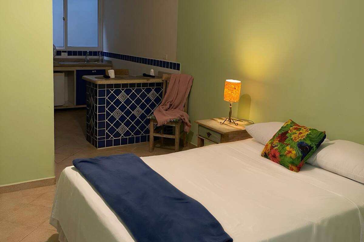 A bedroom with a bed, a nightstand, a lamp, a chair, and a small table.