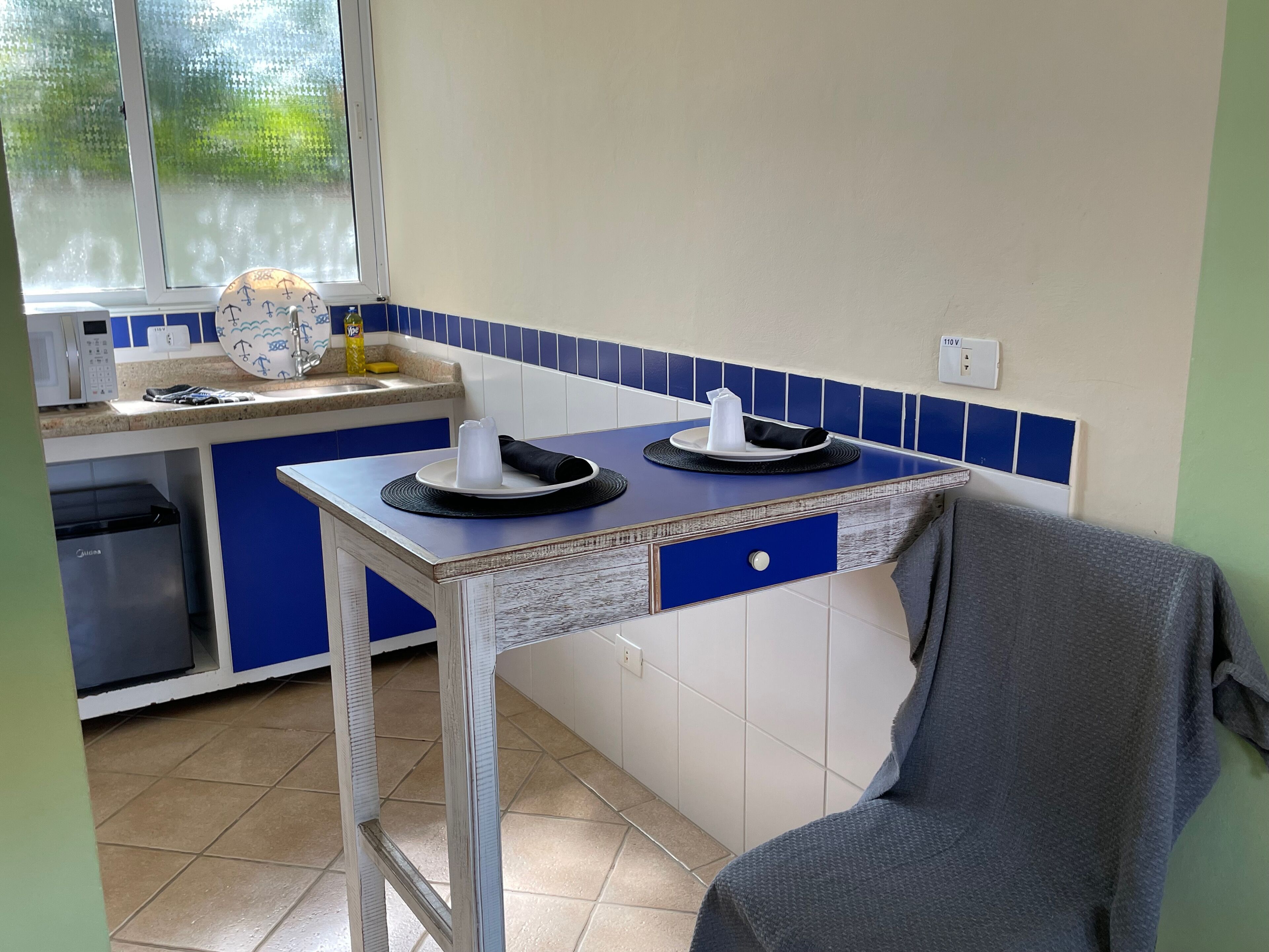 A kitchen with a blue and white color scheme, a microwave, a sink, and a window with frosted glass.