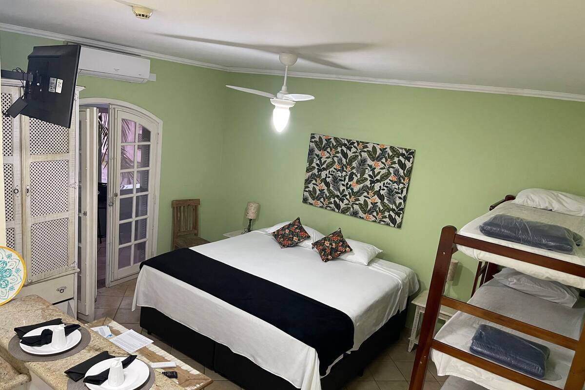 A room with a bed, a desk with a chair, a wardrobe, a ceiling fan, and a wall-mounted artwork.