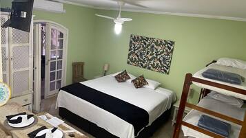 Una habitación con cama, un escritorio y silla, un armario, un ventilador de techo y una obra de arte colgada en la pared.